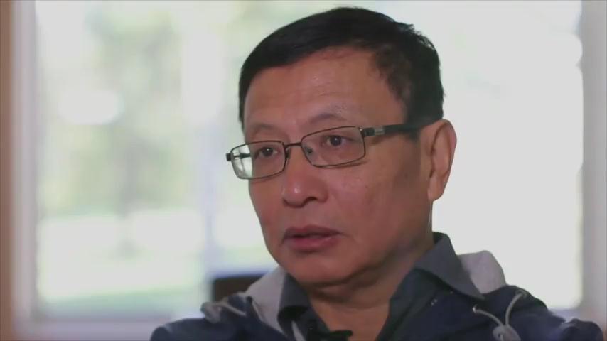 A man with short black hair and glasses, in a dark jacket, looking off to the side during an interview