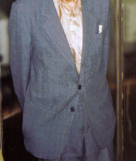 Paul Erdős, white-haired and wearing large glasses and a grey suit, standing in a doorway
