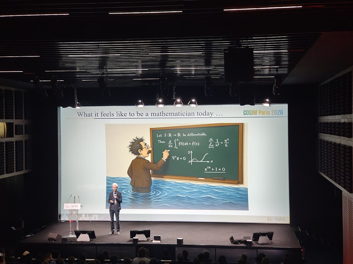 Timothy Gowers speaking on a large stage in front of a projected slide titled What it feels like to be a mathematician today