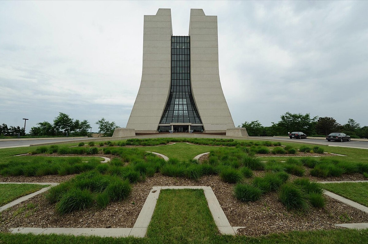 A modern tower with two tall concrete wings joined by a glass center, behind a landscaped lawn