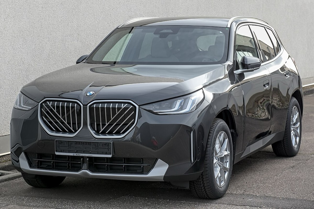 A dark grey BMW X3 of the current generation parked in front of a white wall