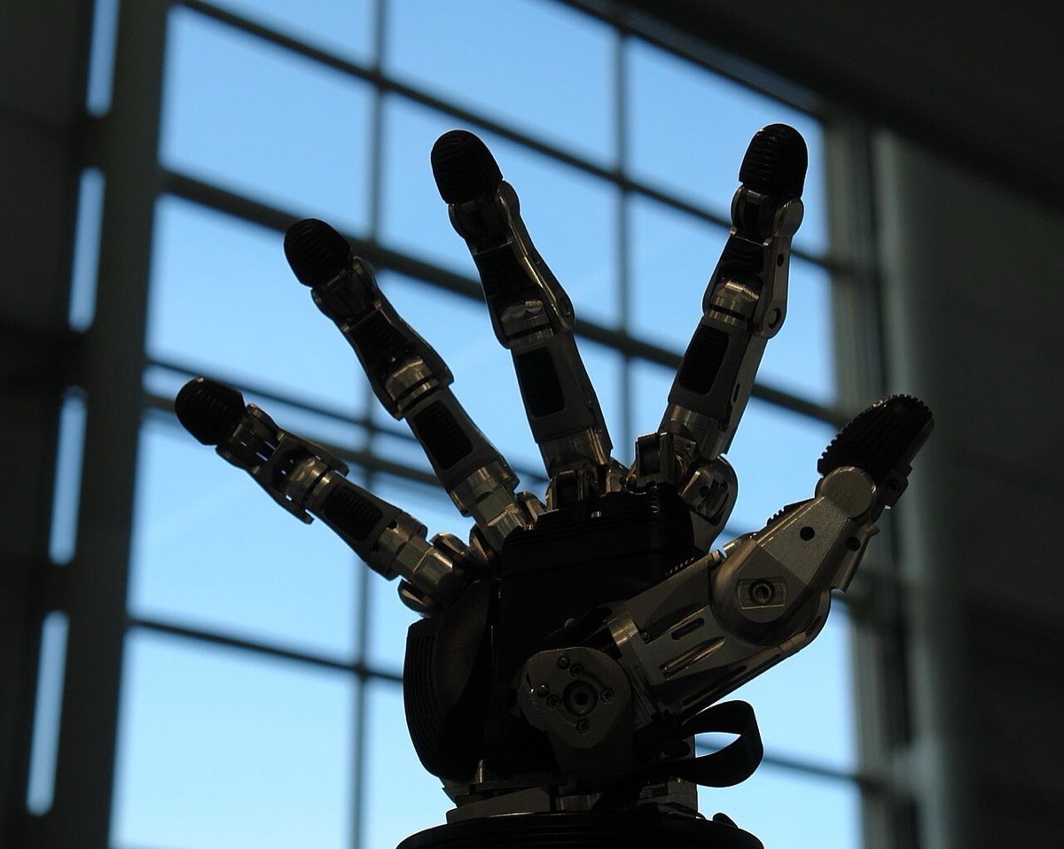 A five-fingered robotic hand with metal joints and black fingertip pads, silhouetted against a window