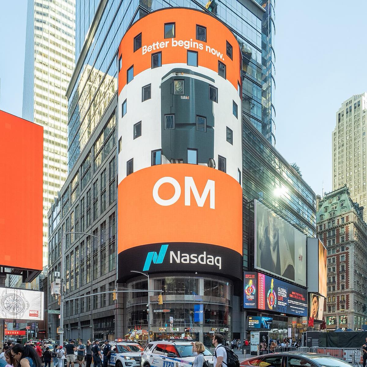 The curved Nasdaq MarketSite tower in Times Square wrapped in a large digital screen, with crowds and police cars on the street below