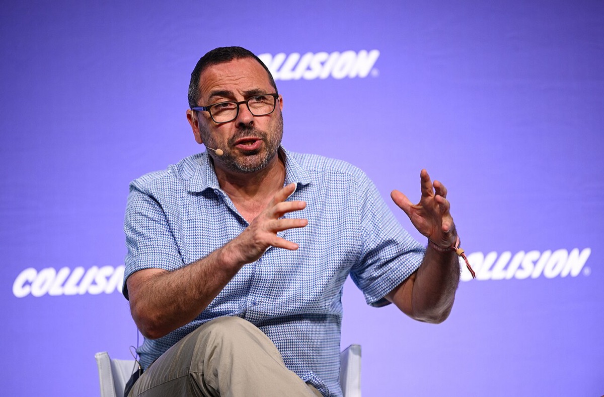 Andrew Feldman, seated on stage, gestures with both hands while speaking at a conference