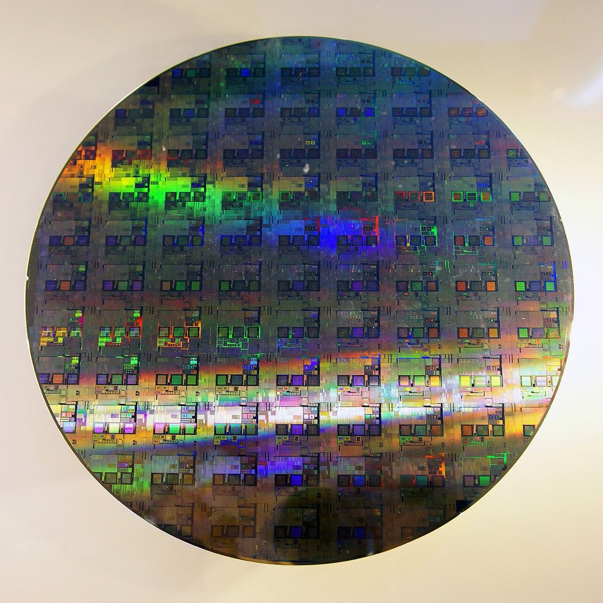 A shiny 12-inch silicon wafer with a grid of many printed chips, reflecting light in rainbow colors