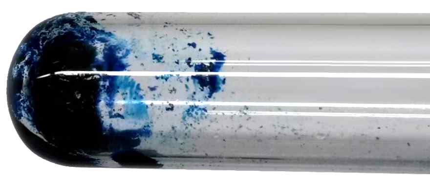 A glass test tube coated inside with patches of deep blue powder
