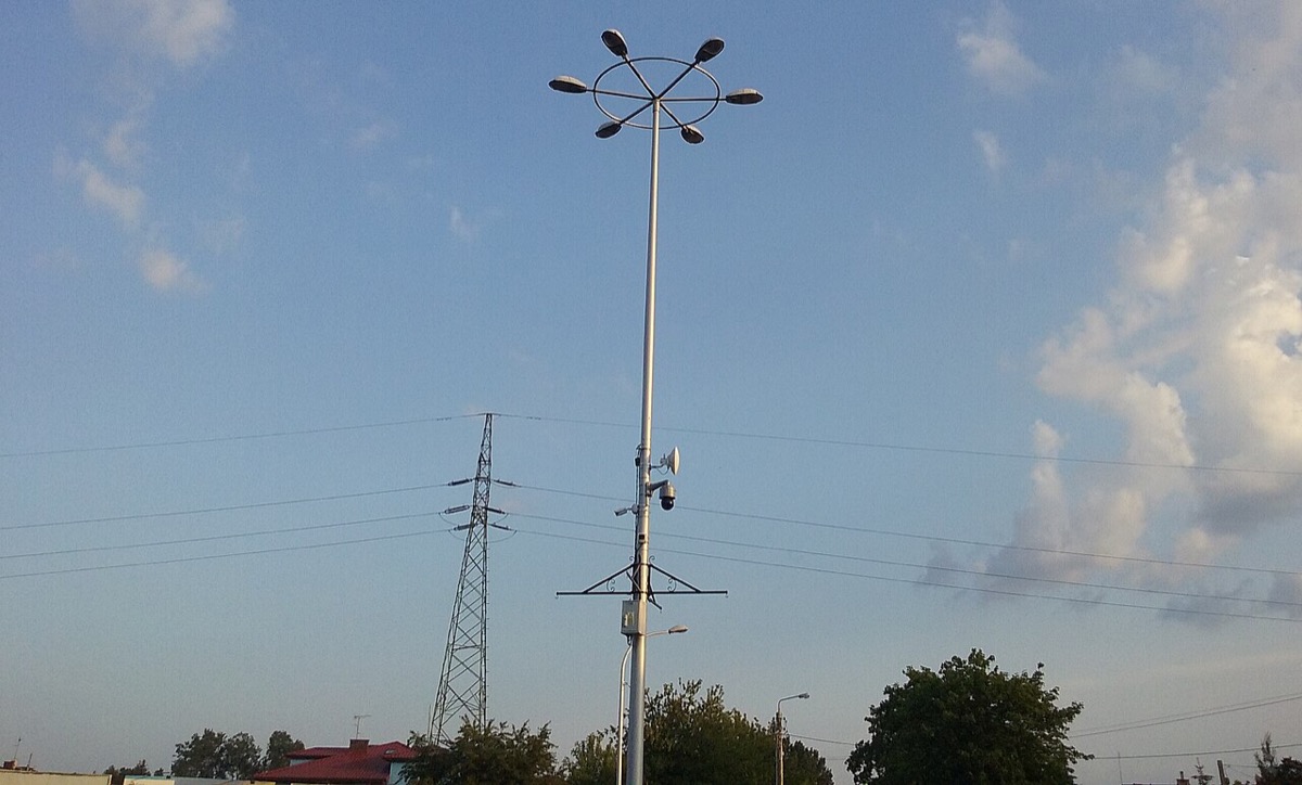 CCTV cameras mounted on a tall street-light pole at a roundabout, against a blue sky with power lines behind