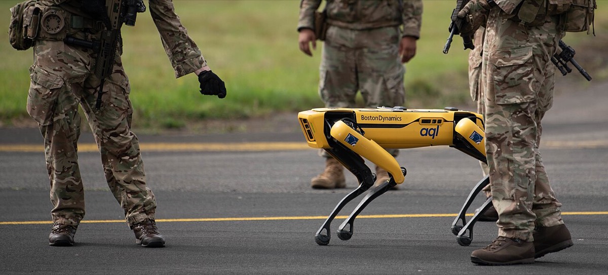 Soldiers in camouflage stand on an airfield around a yellow Boston Dynamics Spot quadruped robot