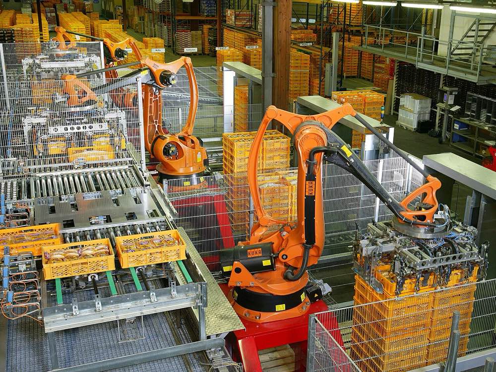 Orange industrial robot arms stacking yellow bread crates on a factory palletizing line