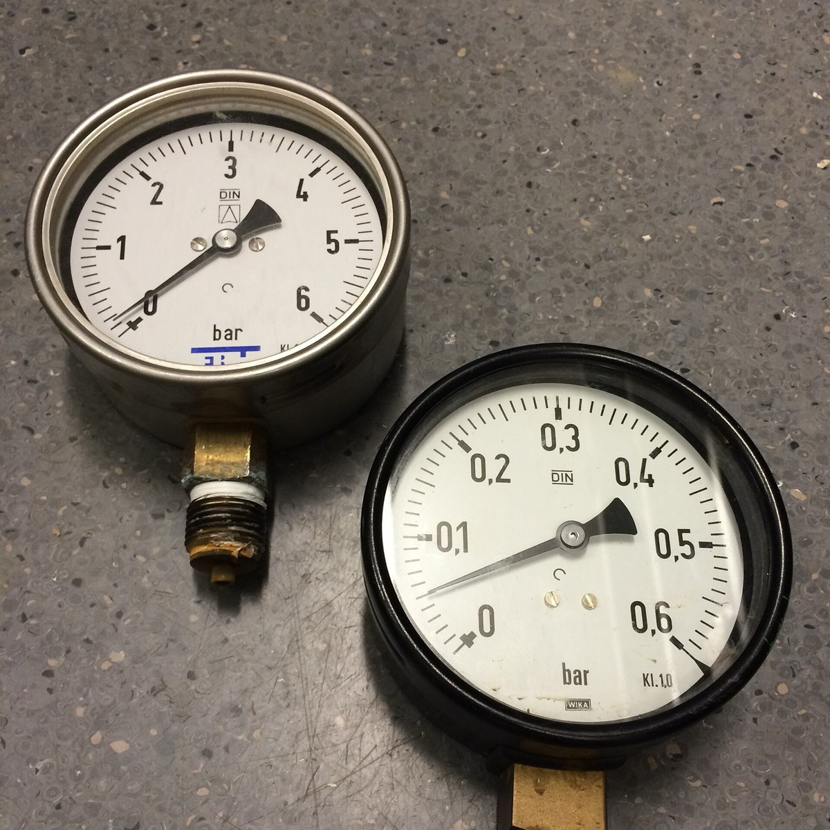 Two round analog pressure gauges with needles and bar scales lying on a gray workbench