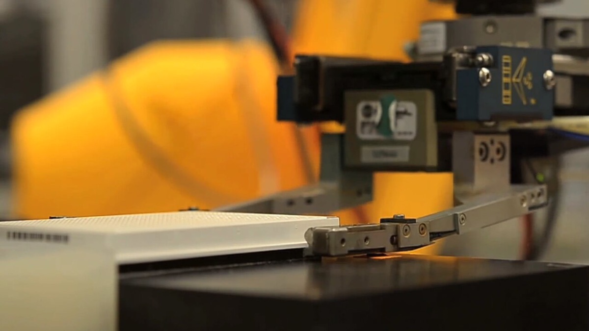 A laboratory robot arm with a gripper lifting a white assay plate during a high-throughput screening run