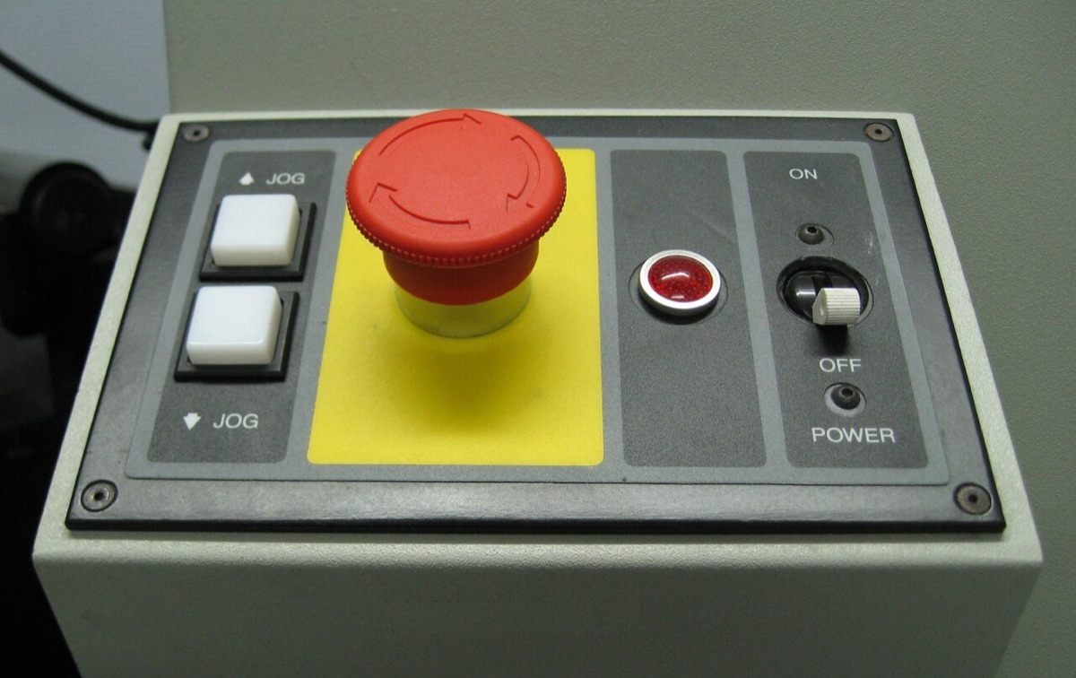 A red emergency stop button on a yellow background, mounted on a laboratory machine's control panel
