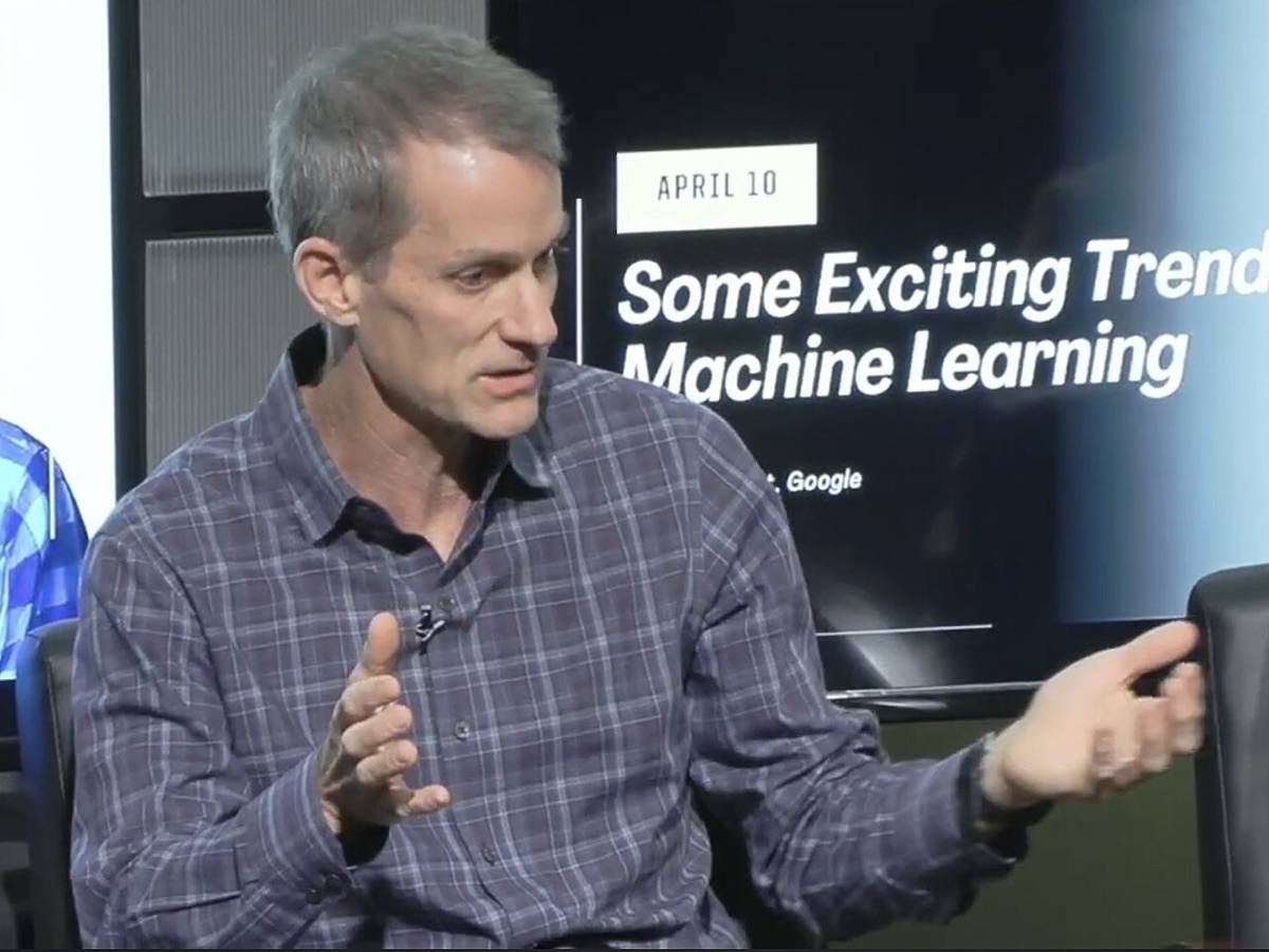 Jeff Dean, in a plaid shirt, gestures while speaking in front of a screen reading Some Exciting Trends in Machine Learning