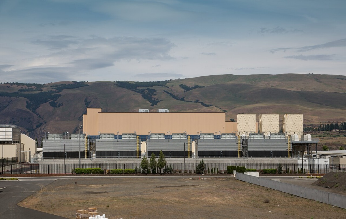 A long, low, beige data center building with rows of cooling units in front of brown hills