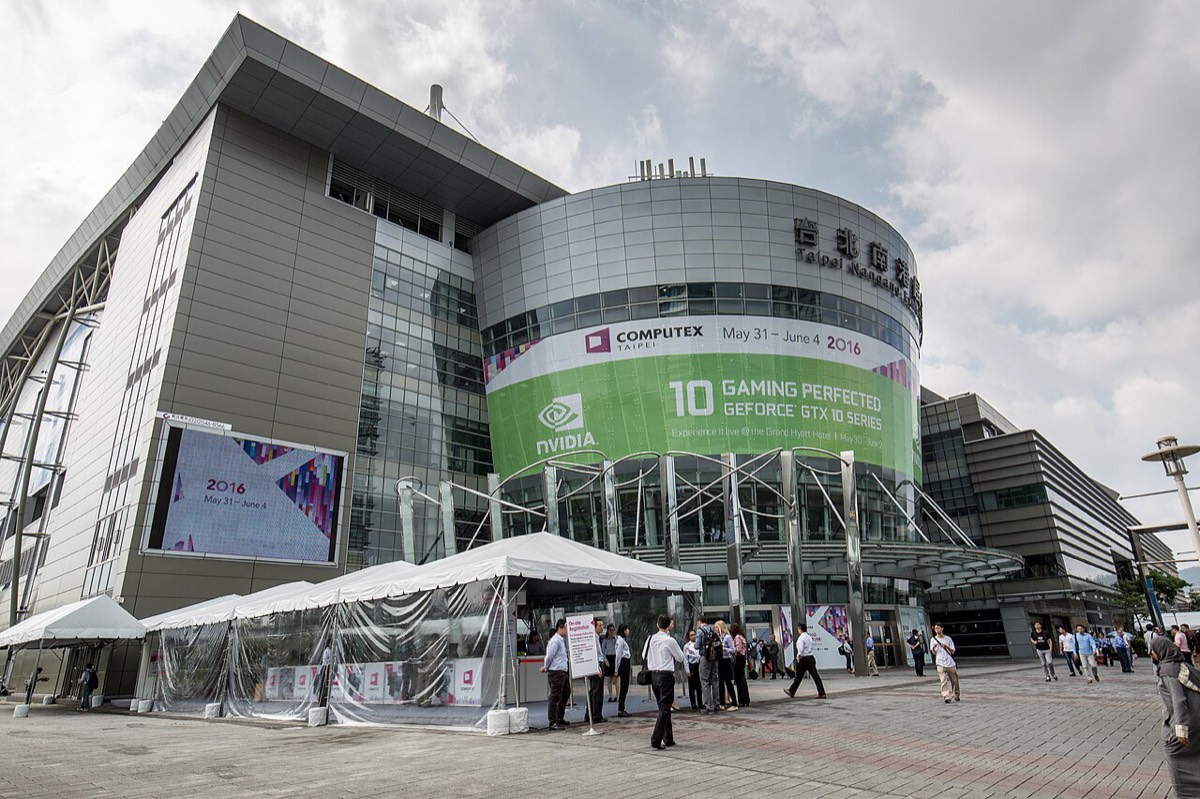 The Taipei Nangang Exhibition Center, a curved glass and metal building, with a large green Computex 2016 banner and visitors walking in front