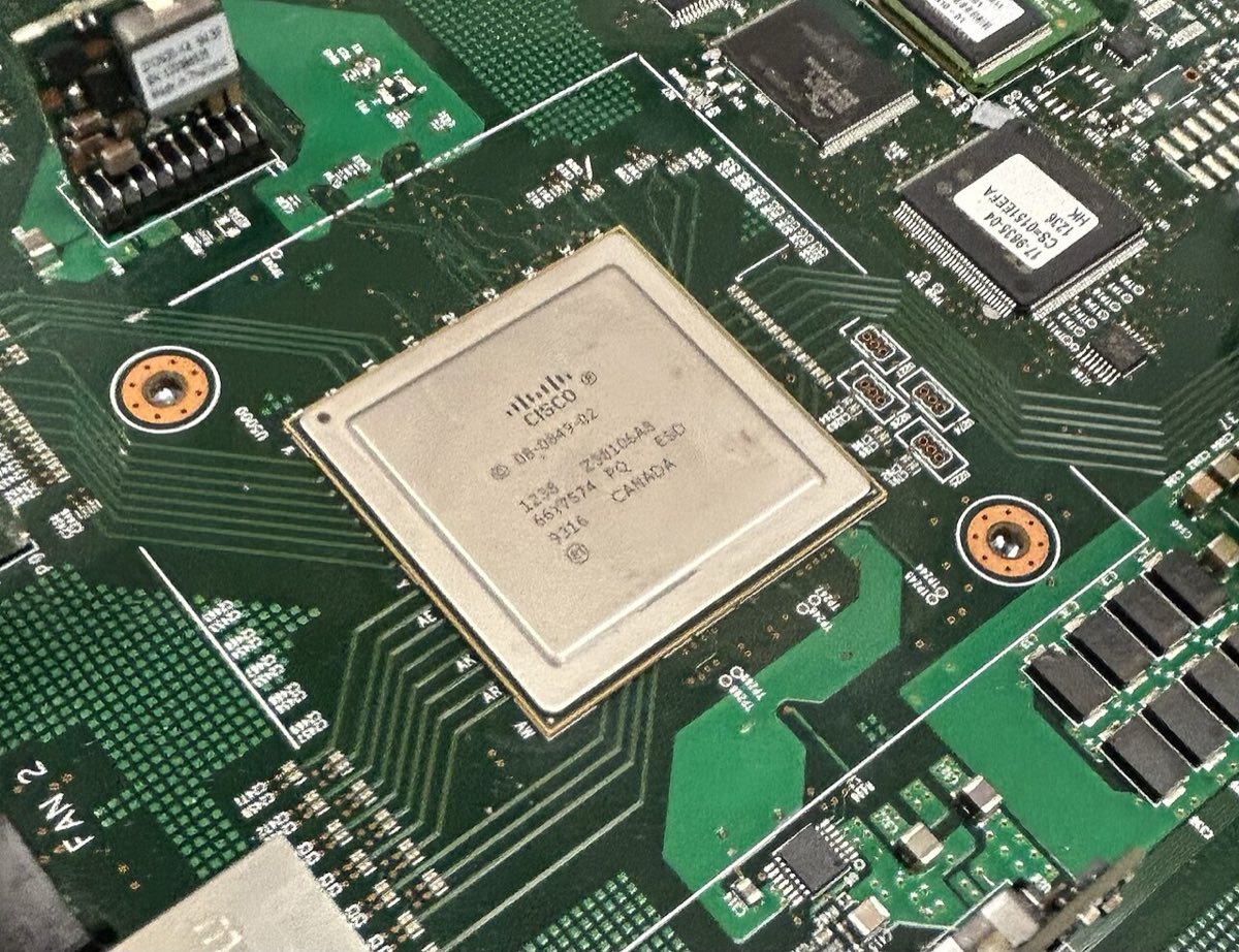 A large silver Cisco packet-processing chip mounted on a green circuit board inside a network switch