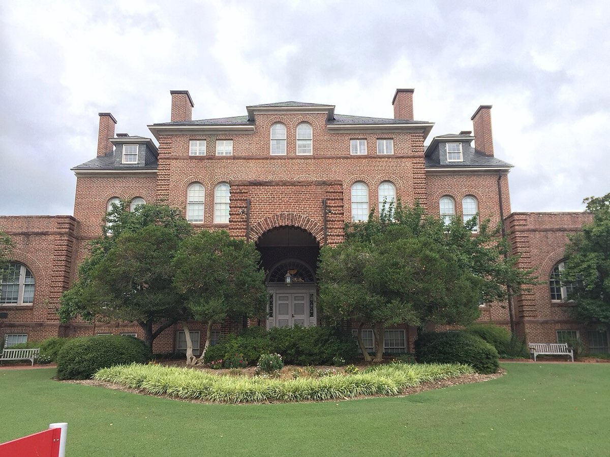 The red-brick front of Holladay Hall behind a lawn and shrubs under a cloudy sky