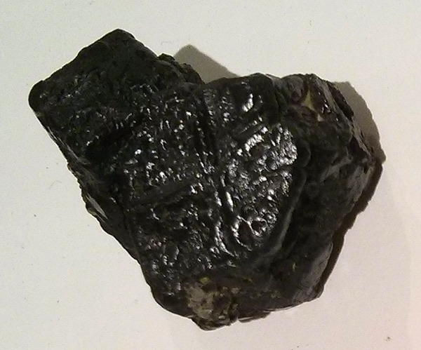 A rough, dark, faceted mineral specimen on a white background