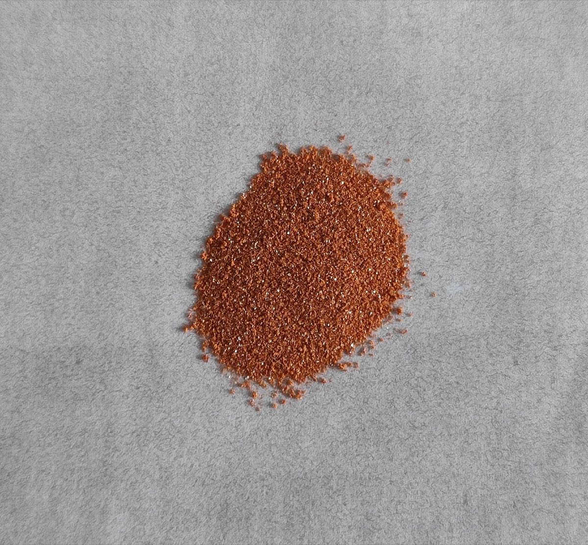 A small pile of orange crystalline powder on a grey surface