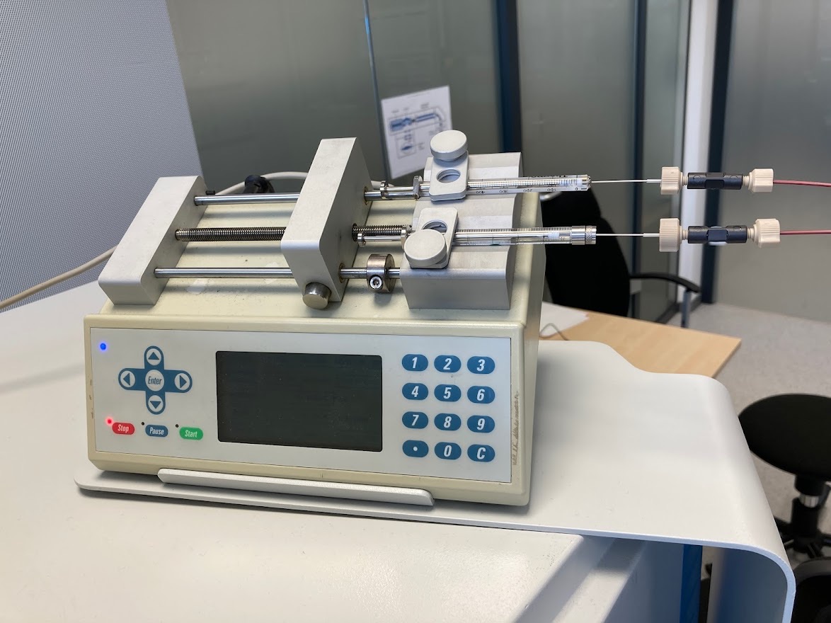 A beige syringe pump with a keypad and screen, holding two glass syringes connected to thin tubing