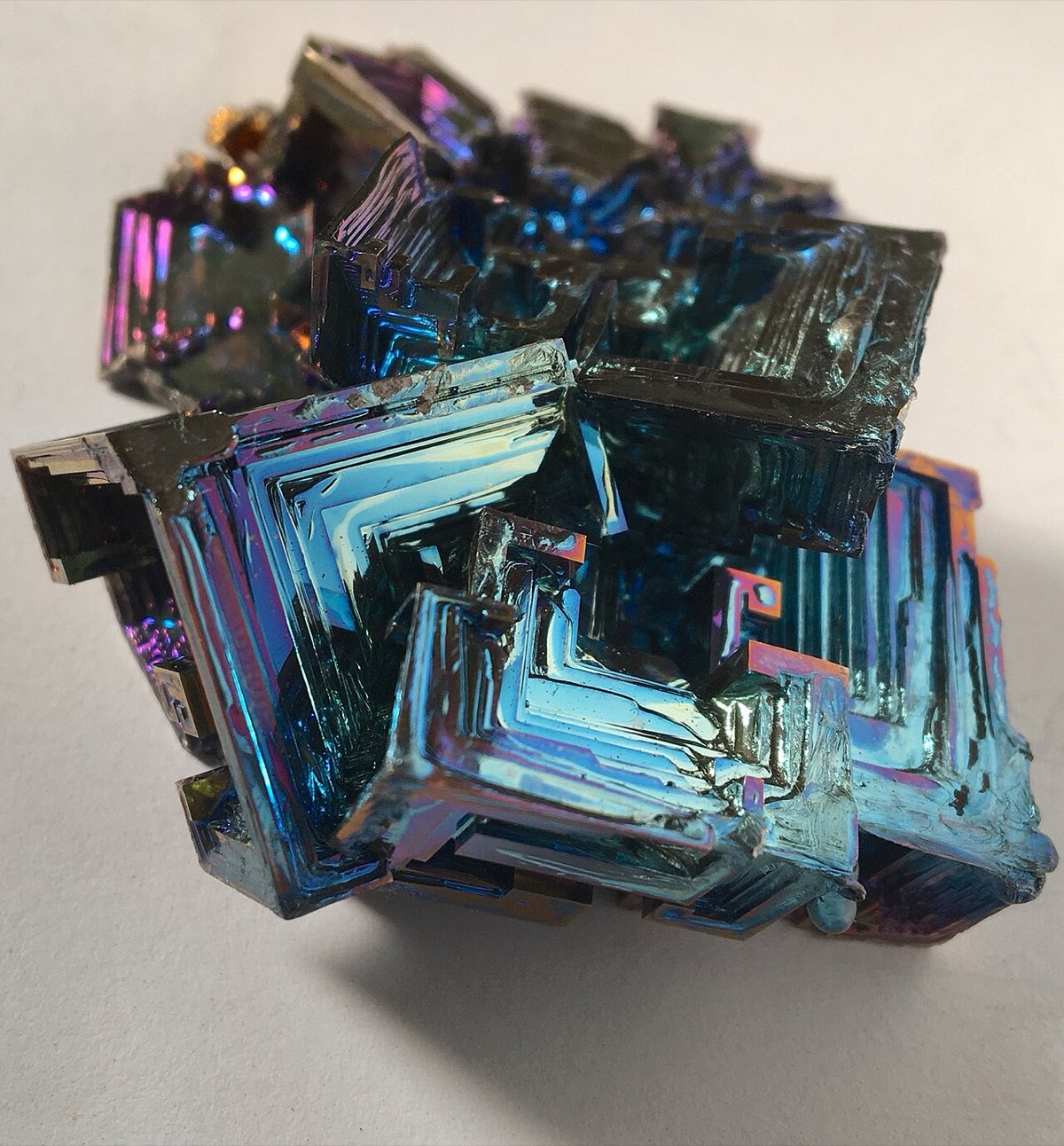 A metallic bismuth crystal with stepped, hollow square faces and iridescent blue and purple oxide colors