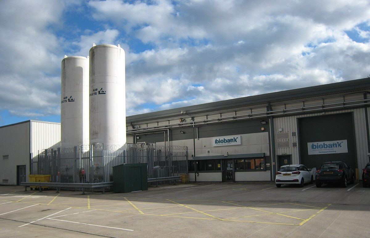 A modern building with a curved glass entrance and two tall white storage tanks, the UK Biobank headquarters in Stockport