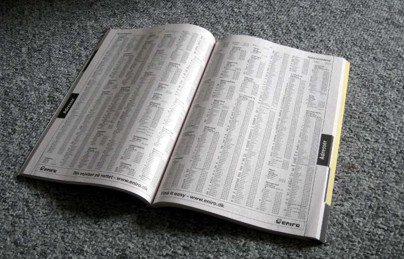 An open telephone directory lying on a grey carpet, its pages filled with dense columns of names and numbers