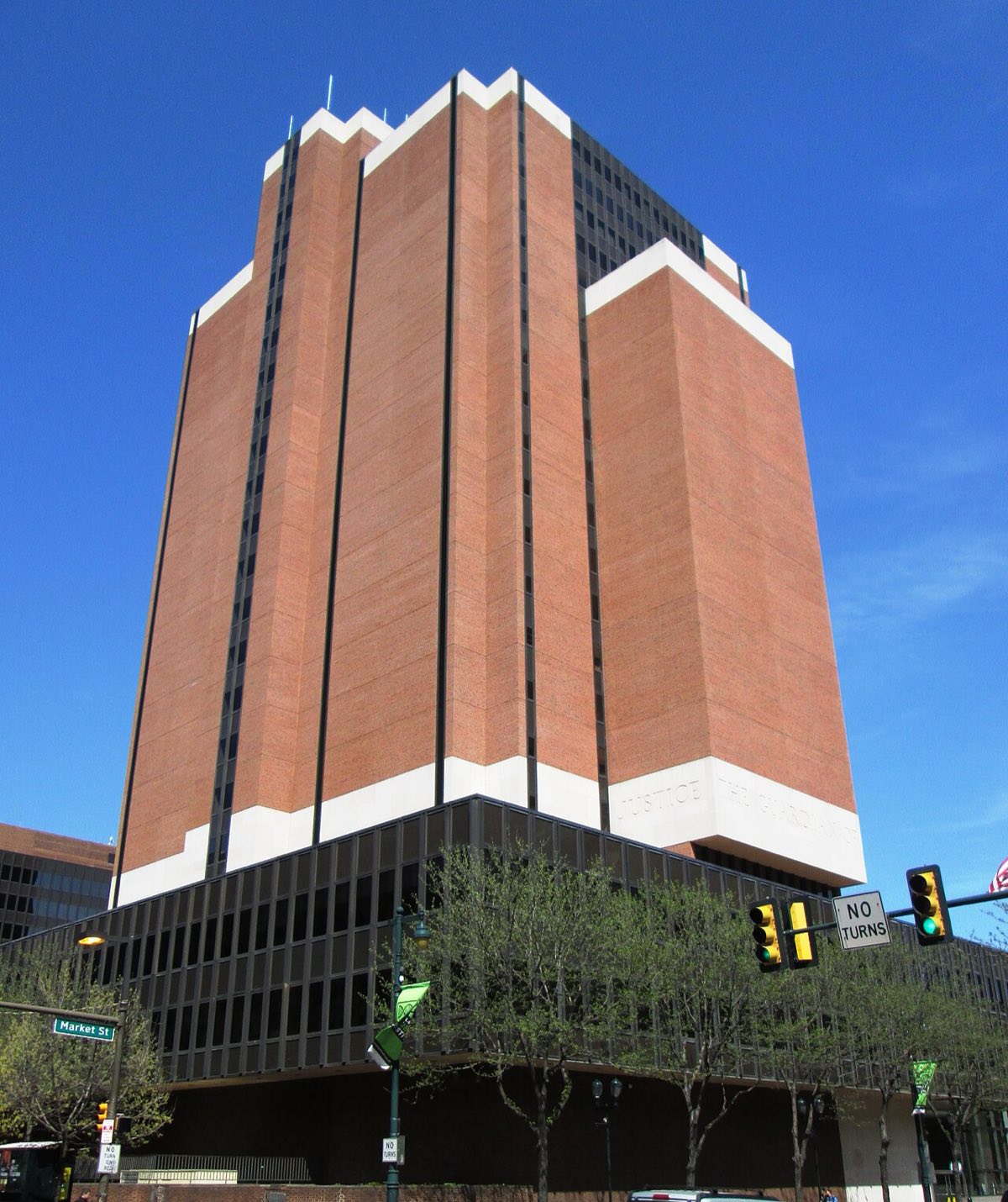 A tall modern office tower of pale concrete and dark windows on a Philadelphia street corner, with trees in front