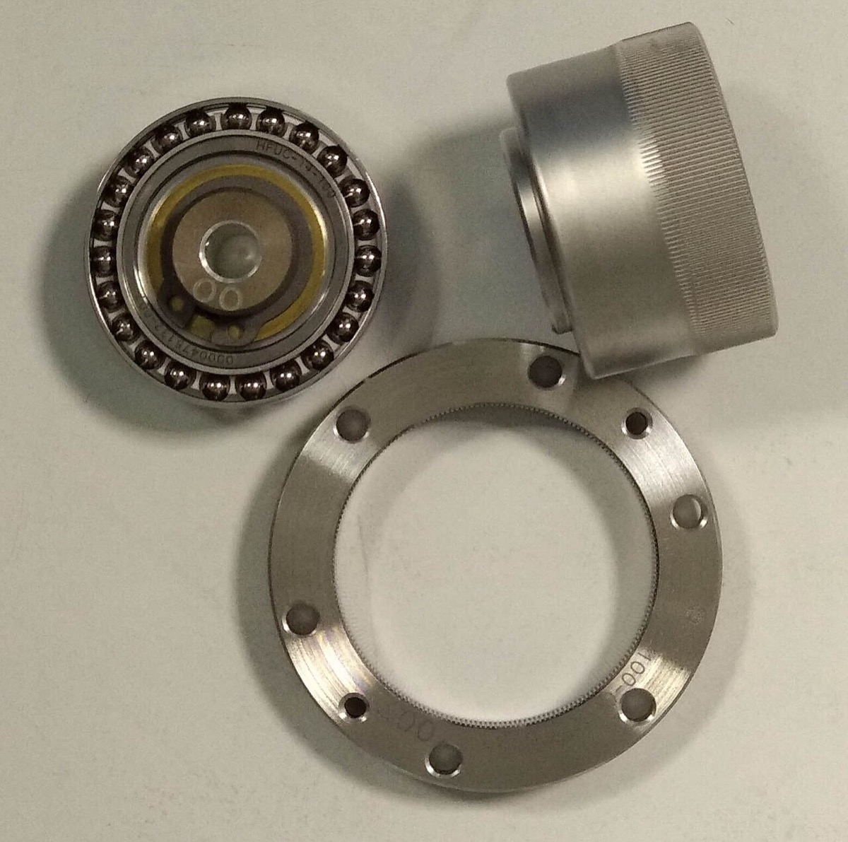 A disassembled strain wave gear set: a ring, a flexible metal cup and an oval bearing on a table