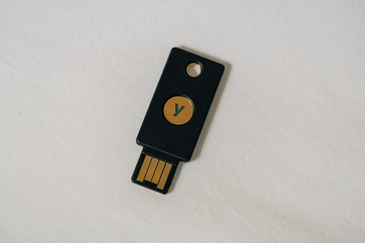 A black hardware security key with a gold contact and button lying on a white surface