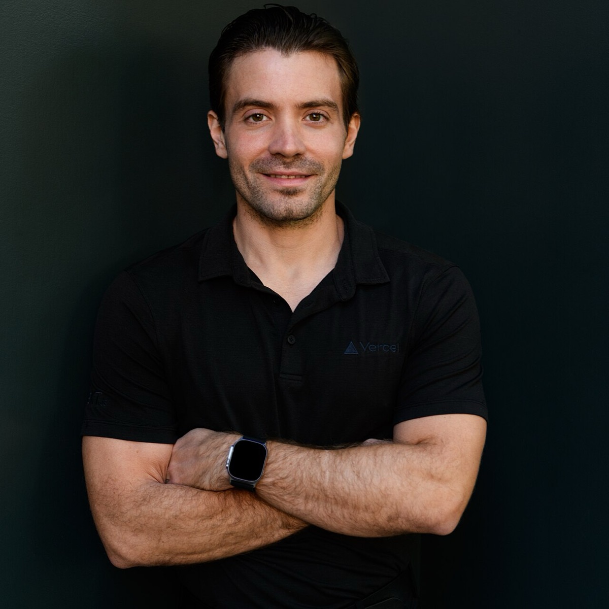 Guillermo Rauch, Vercel's chief executive, standing with arms crossed in a dark polo shirt against a black background
