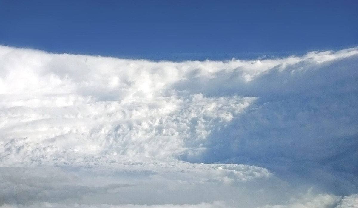 The towering white wall of clouds around a hurricane's eye, seen from inside the eye against a blue sky