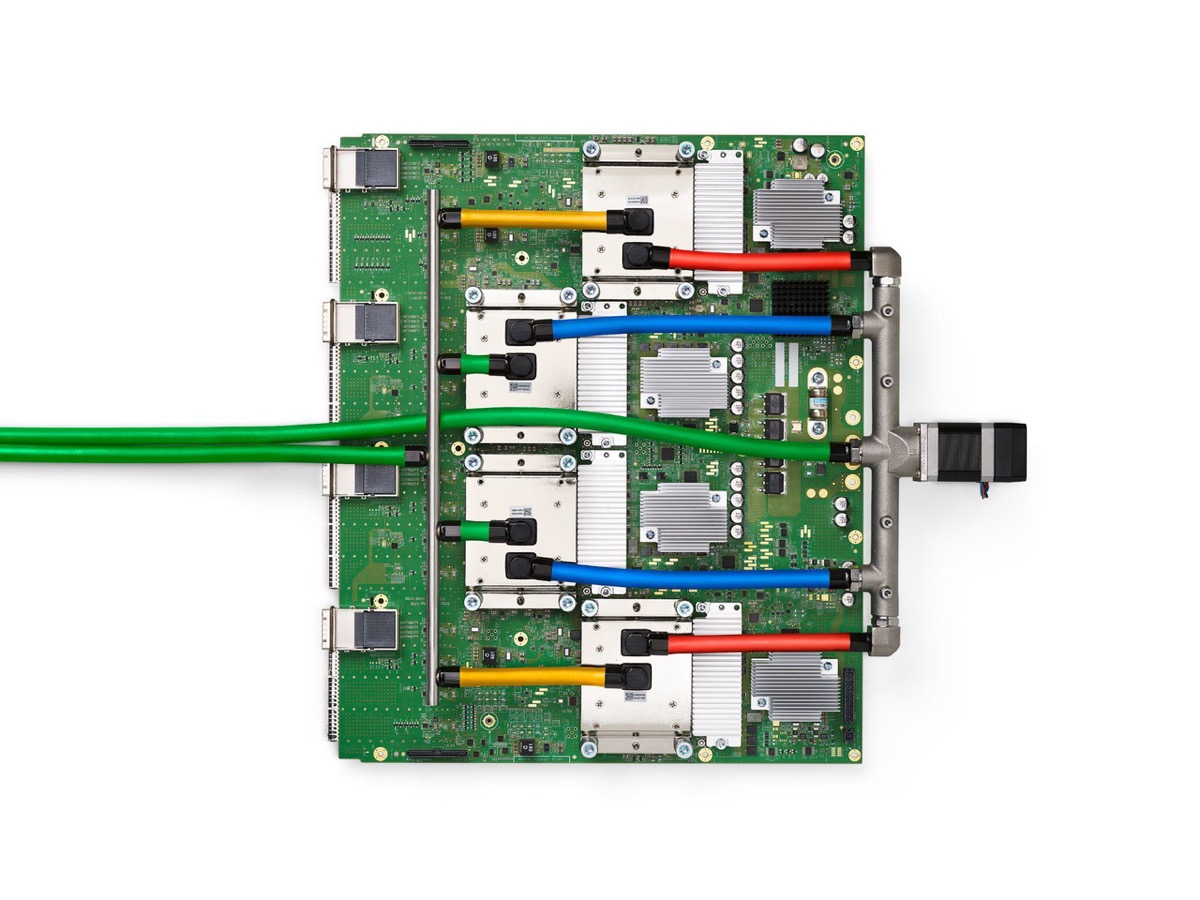 A green circuit board with four liquid-cooled processor packages connected by colored coolant hoses